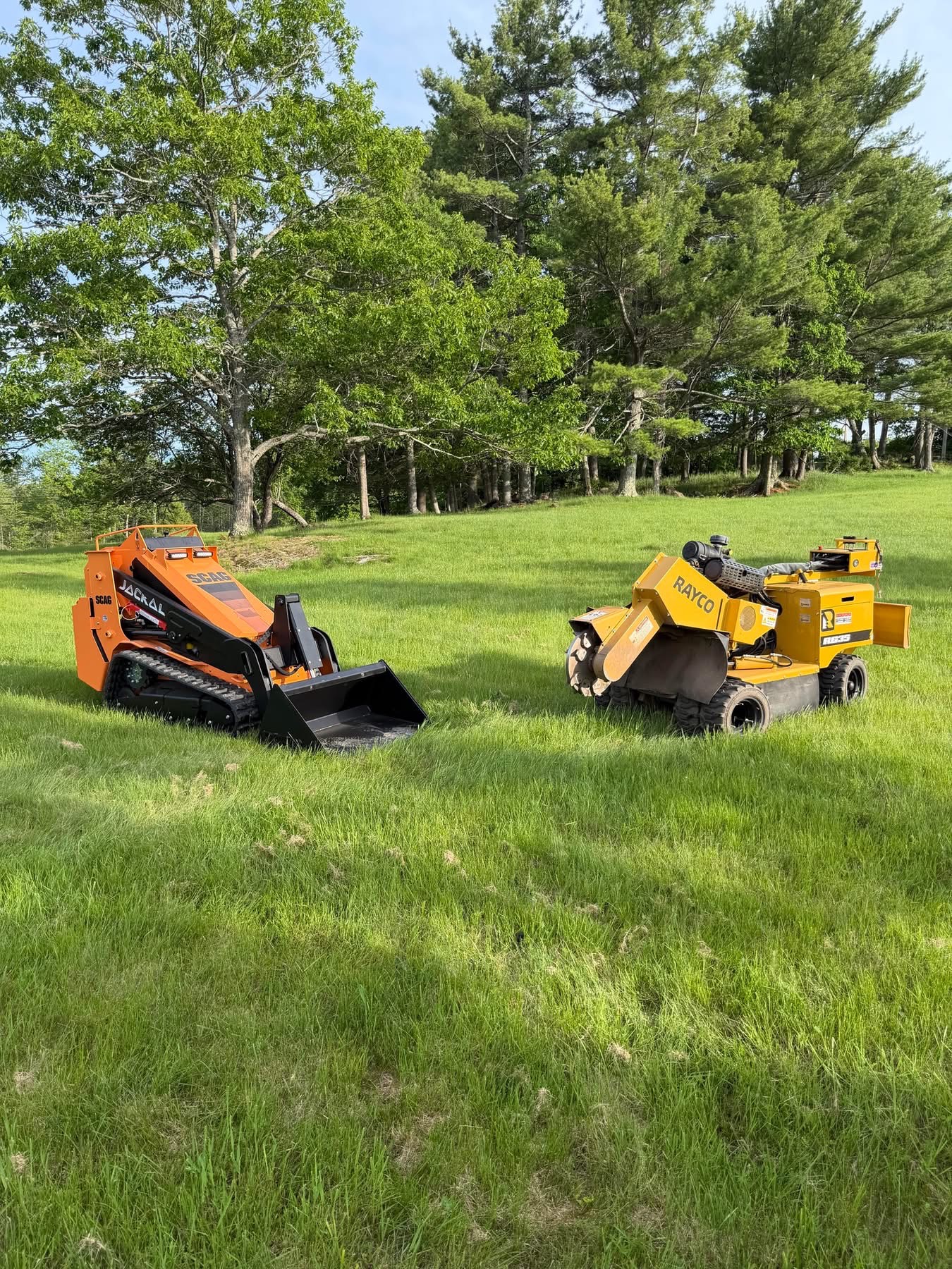 Skid steer and stump grinder staged in a grassy field